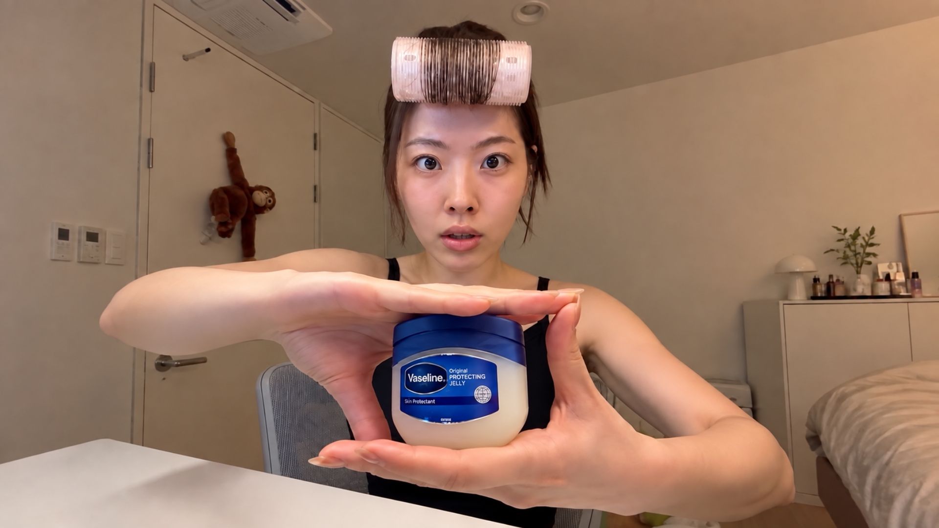 Woman with a hair roller holds a jar of Vaseline against a blue background.