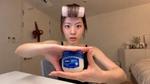 Woman with a hair roller holds a jar of Vaseline against a blue background.