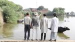 A overflowing dam with farmers standing and looking at the surplus.