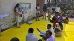 Facilitator leads an outdoor training session with villagers seated on a yellow mat