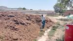 Worker rakes a large mound of soil at a rural agricultural site.