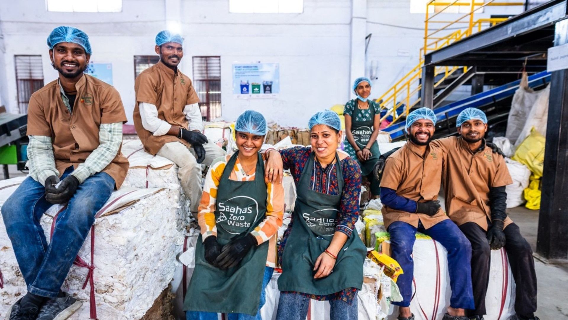Waste processing team wearing protective hairnets poses together inside a recycling facility.