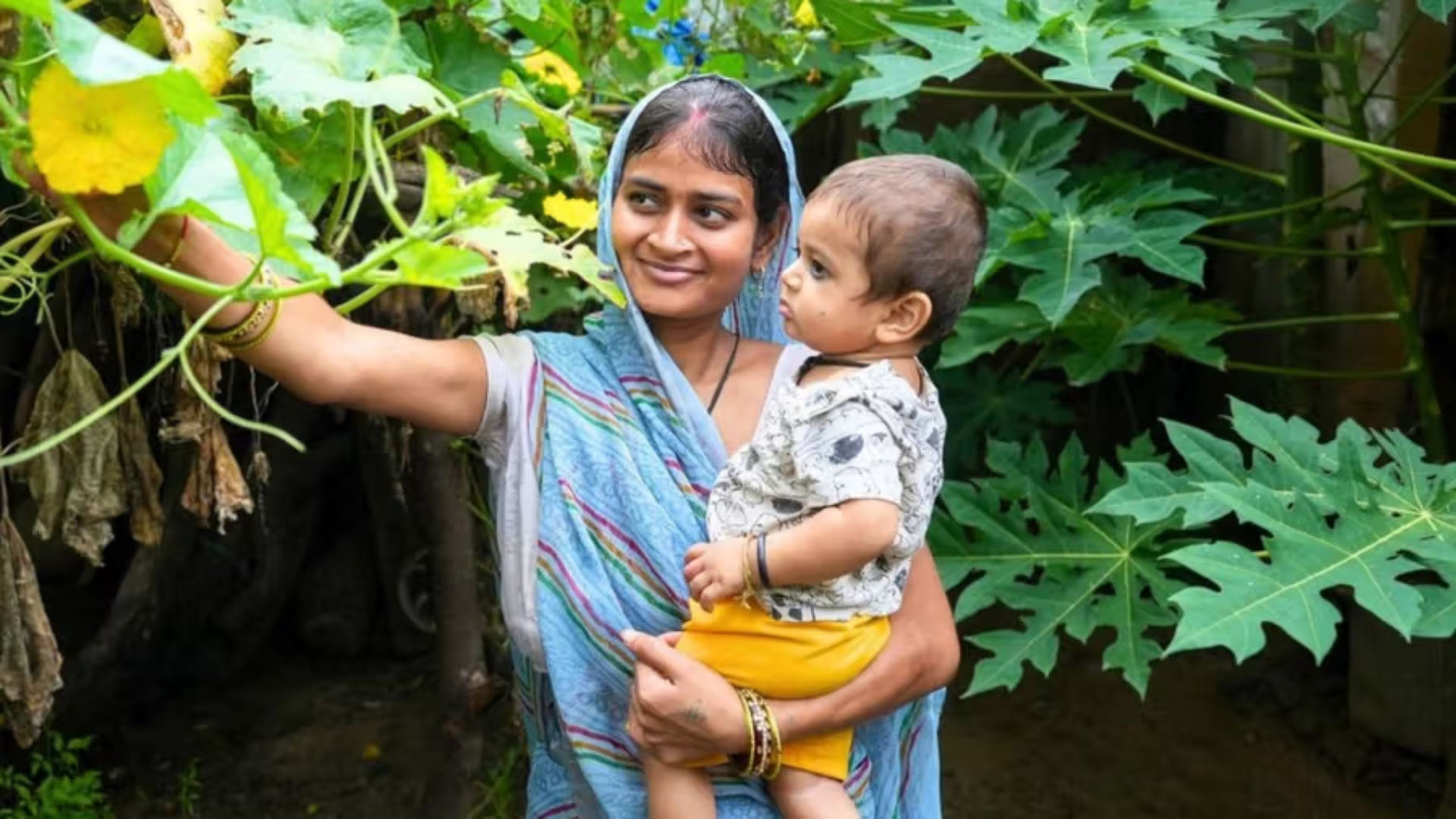 A woman carrying a baby while showing trees