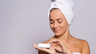 A woman in a towel smiling while holding a bar of soap.