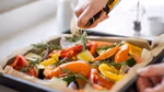 A person pouring olive oil over a roasting pan full of vegetables