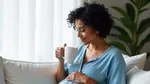 A pregnant woman sitting on a sofa, smiling and holding a mug.