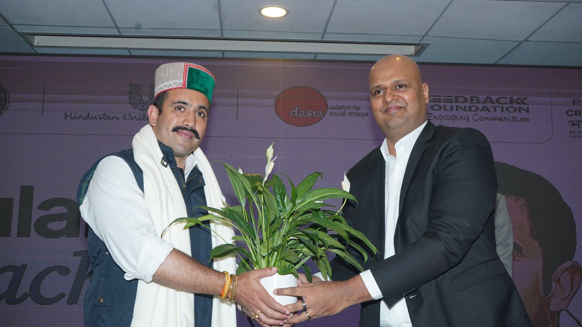 Two men present a potted peace lily during the HUL and Himachal Pradesh collaboration event on waste circularity.