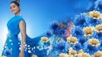 A woman in a flowing blue dress stands against a bright blue background, smiling. Blue and yellow flowers and petals blend into the scene, creating a dreamy and vibrant atmosphere.