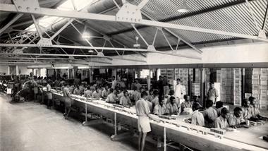 Workers operate a long production line in a large industrial factory.