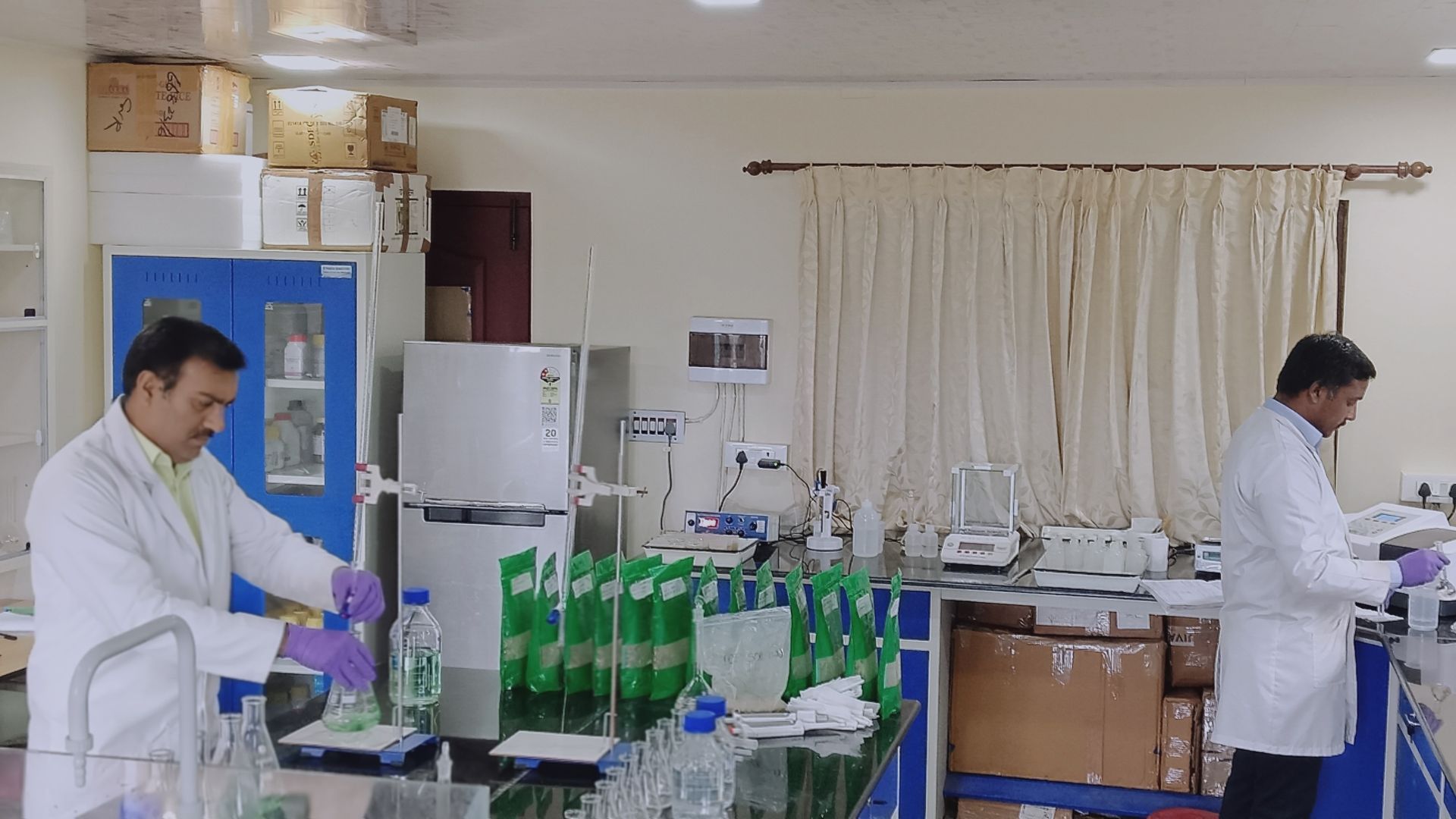 Two scientists in lab coats and gloves conduct tests in a laboratory.