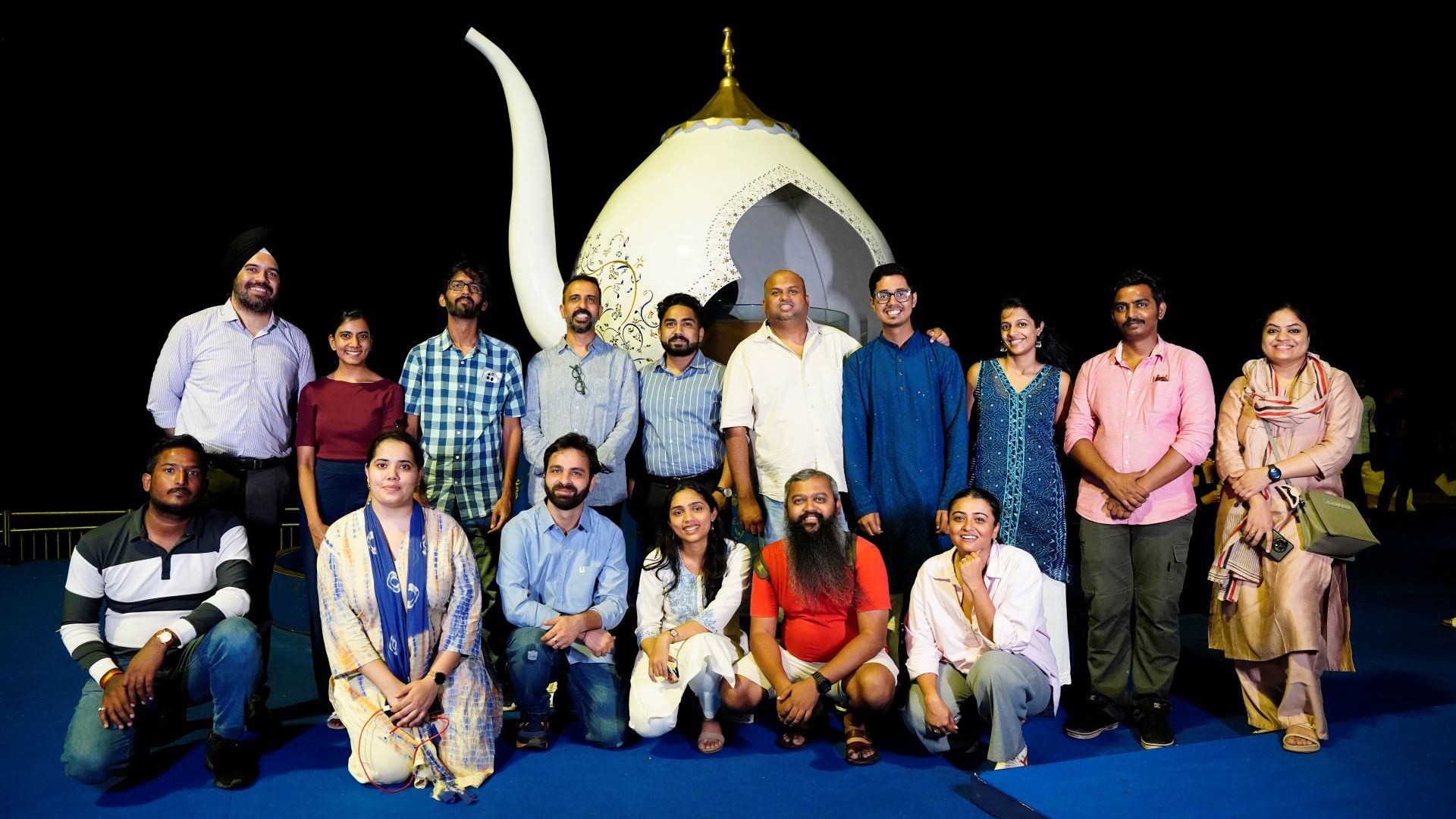 A group of people posing for a photo in front of a big teapot.