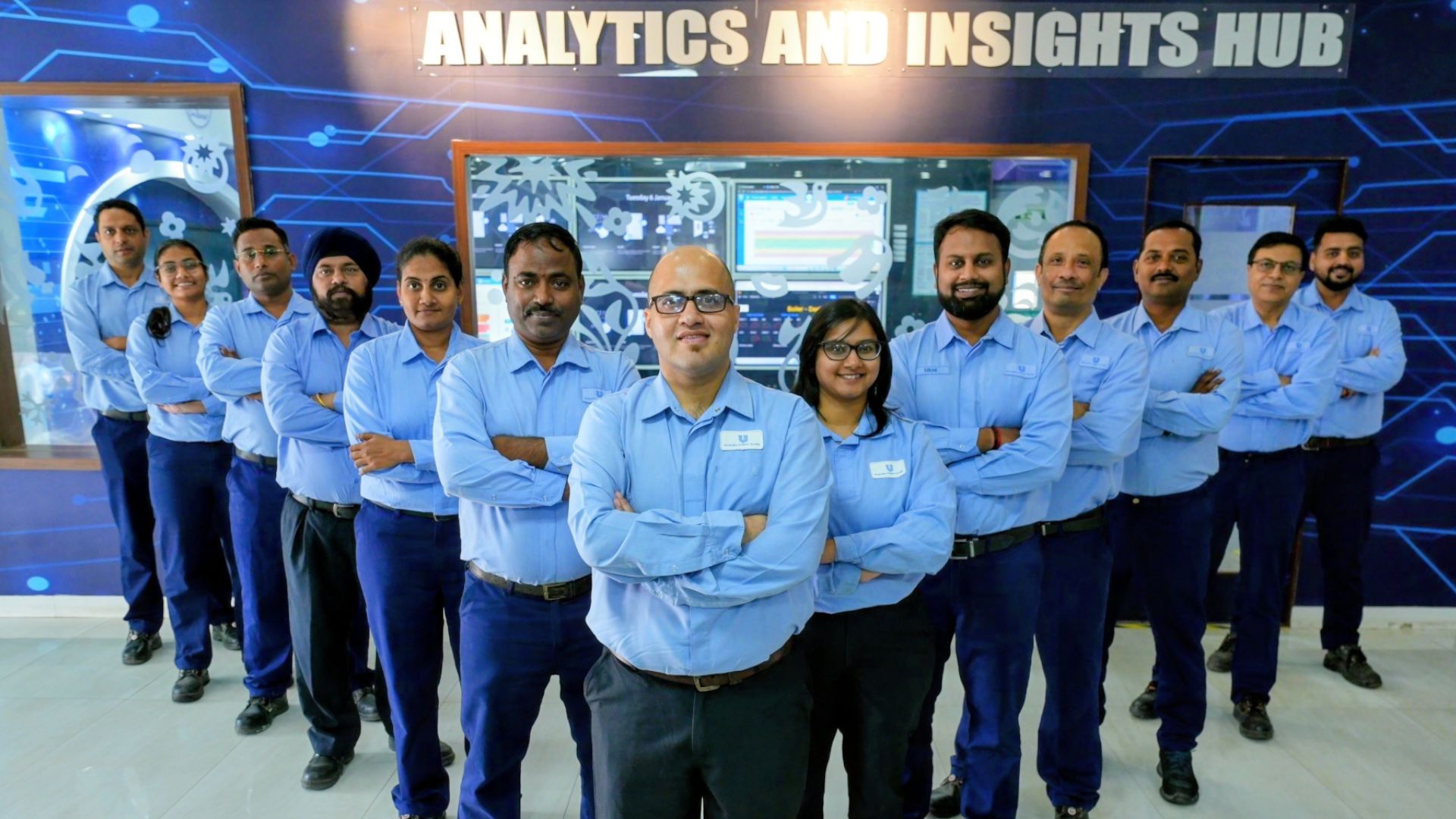 Team of employees in blue uniforms standing confidently in front of an analytics and insights hub.