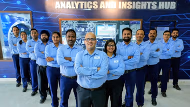 Team of employees in blue uniforms standing confidently in front of an analytics and insights hub.