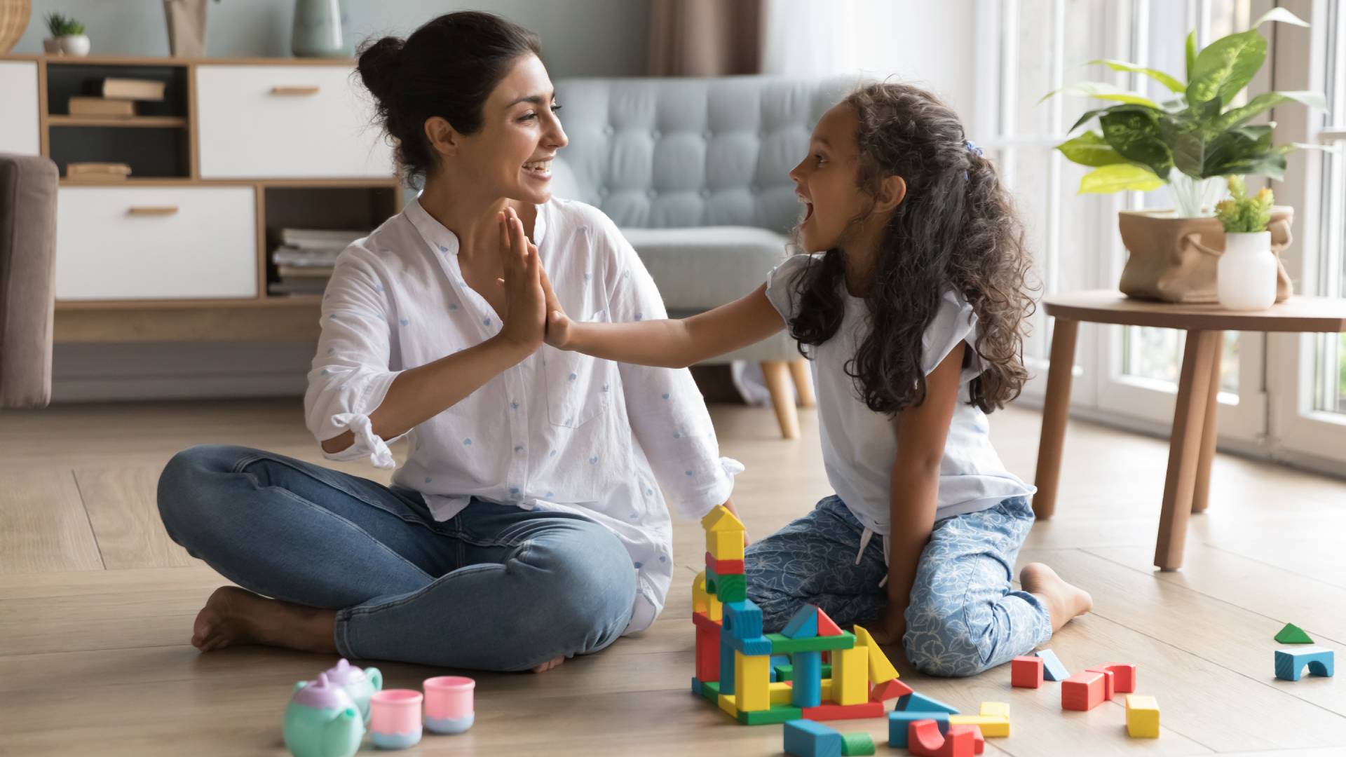 A woman and her daughter joyfully building a tower with colorful toy blocks on a play mat.
