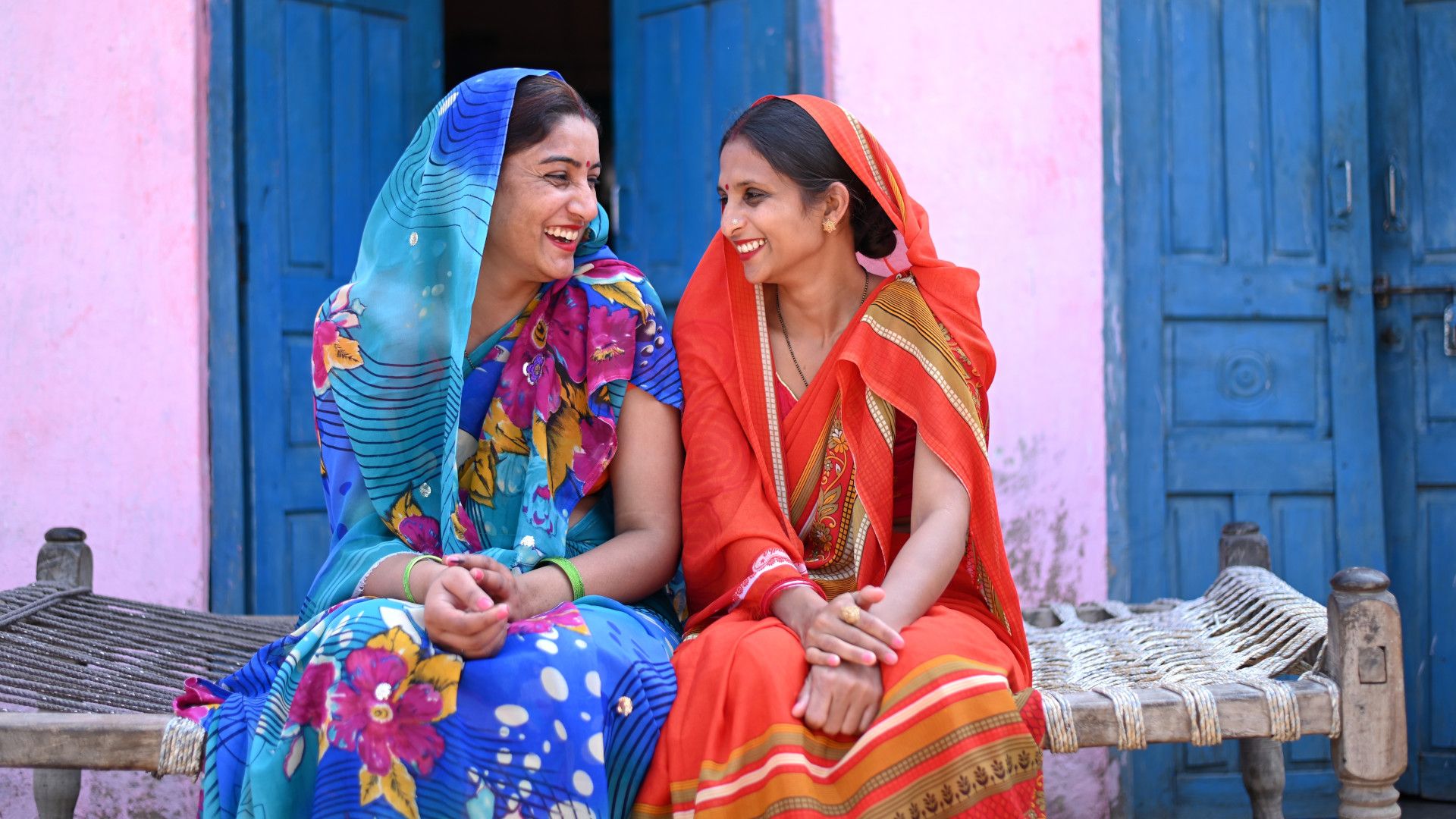 Two Indian woman in colorful saris looking at each other smiling