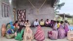 Community members sit in a circle for a group discussion outside a rural home.