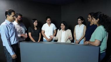 Colleagues gather around a display as a woman leads a workplace discussion.