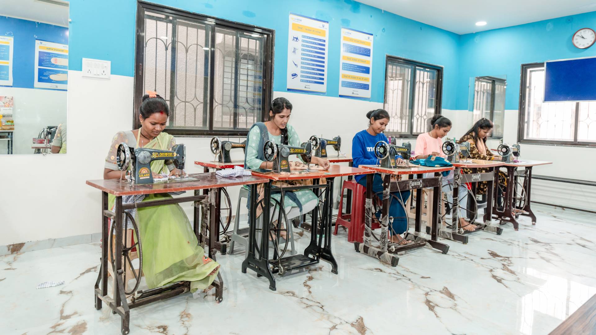 Women sewing at machines in a bright classroom.