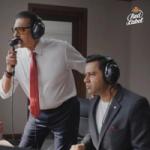 Two men wearing headphones are engaged in a recording session with a microphone.