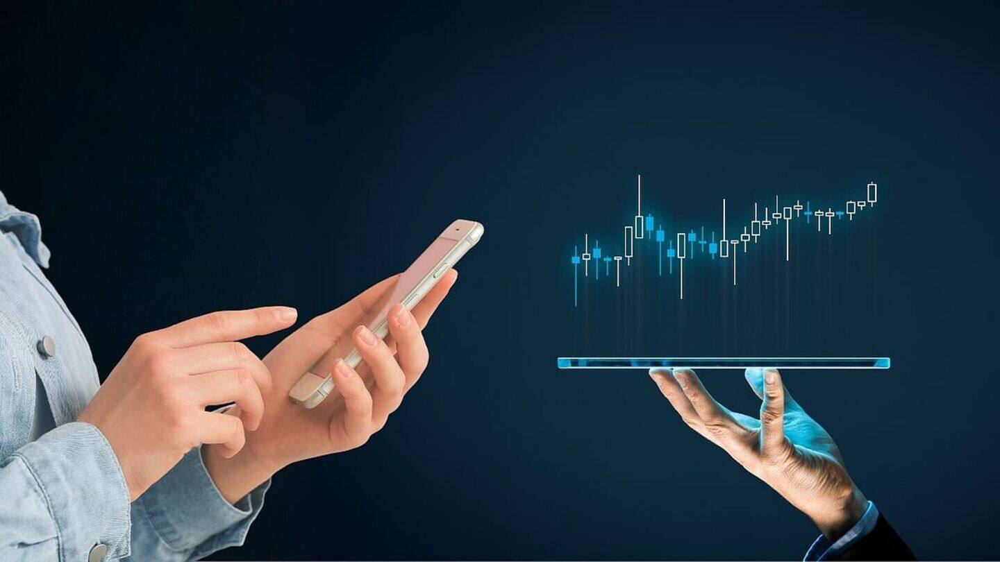 A person uses a smartphone while another hand holds a tablet displaying a digital financial chart.