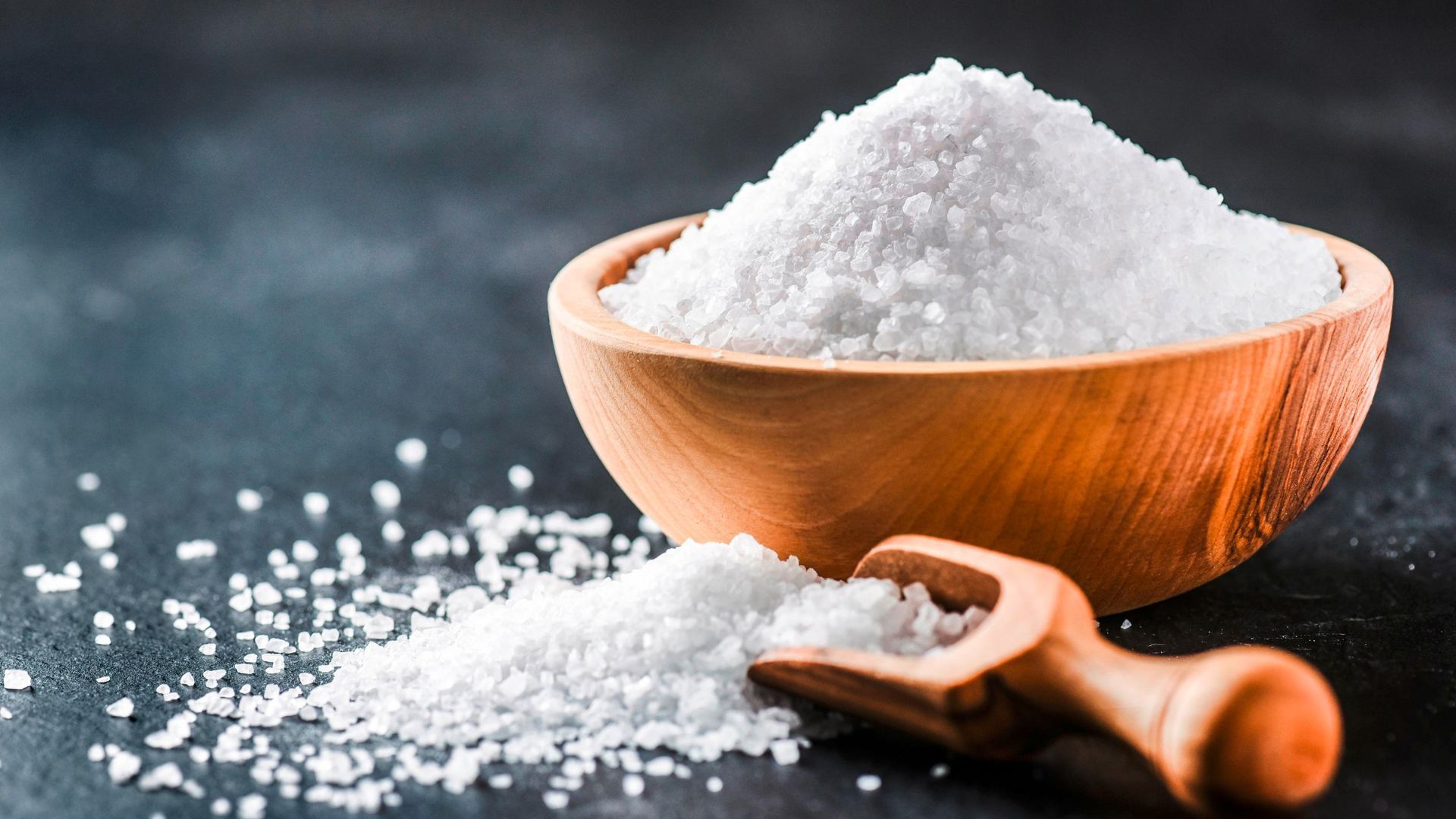 A bowl of coarse salt and a wooden scoop of salt next to it