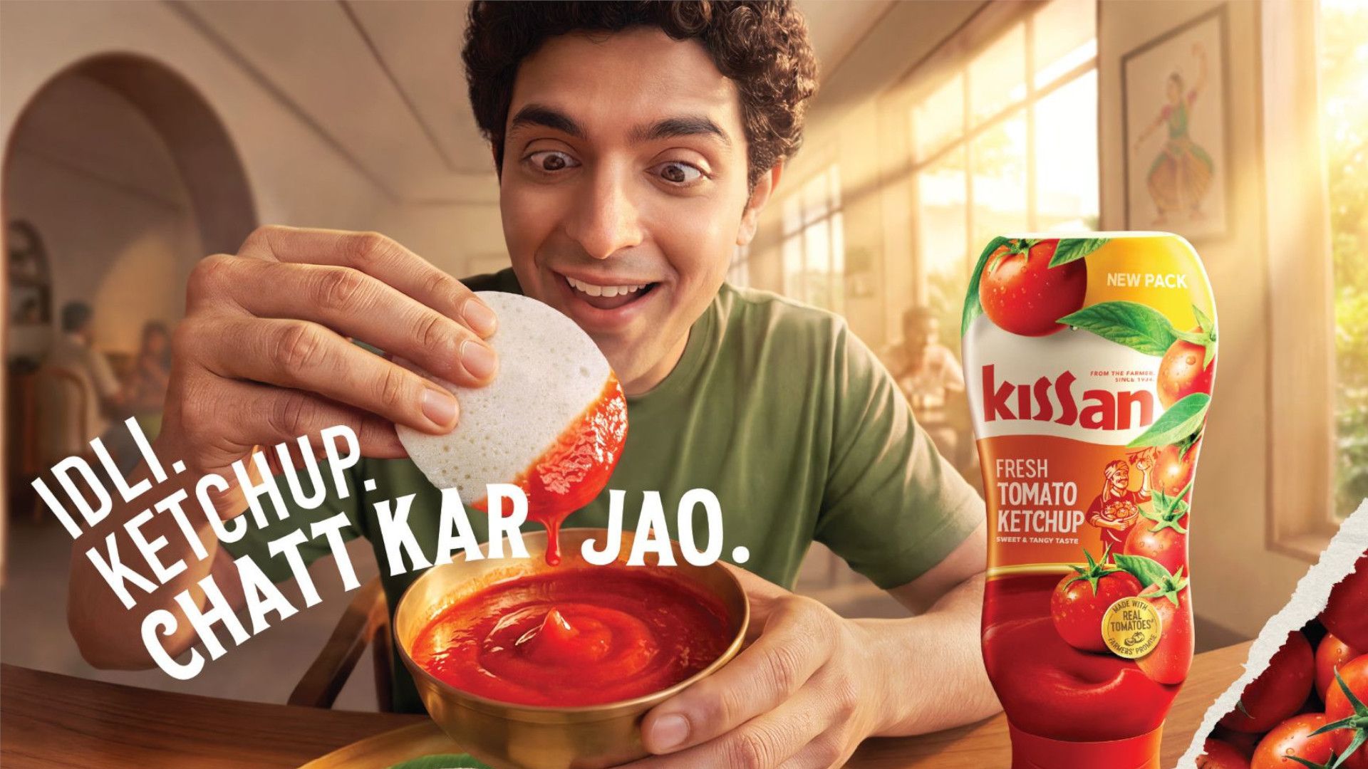 Smiling man dips idli into tomato ketchup beside a bottle of Kissan Fresh Tomato Ketchup.