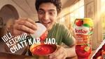 Smiling man dips idli into tomato ketchup beside a bottle of Kissan Fresh Tomato Ketchup.