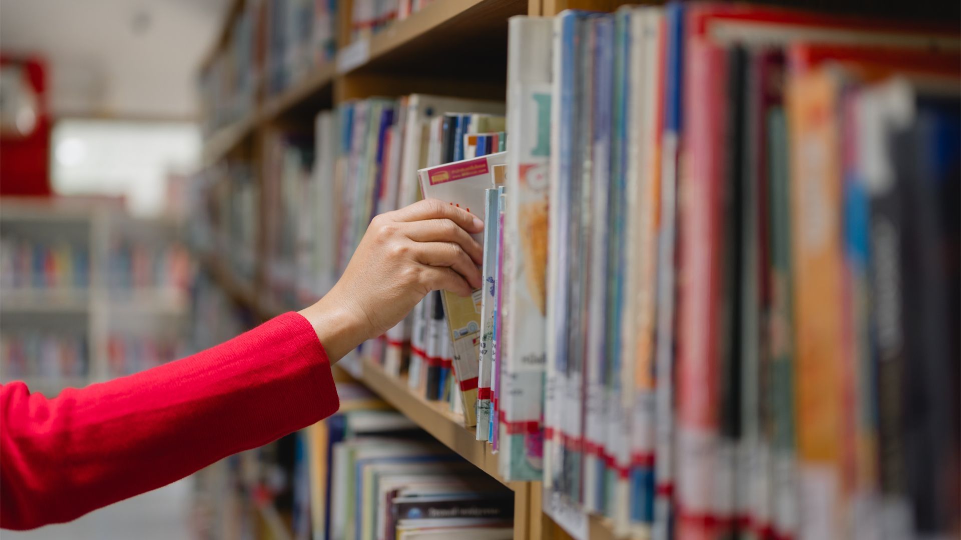 A woman reaching for a book from a full shelf in a library