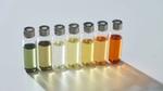 A row of seven glass vials with silver caps. They are filled with green, yellow, amber and colourless perfume samples.