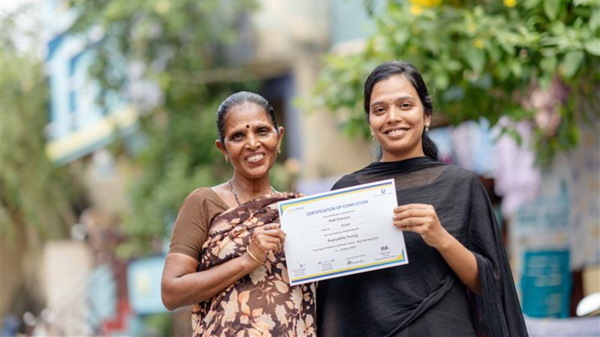 Two smiling women holding a certificate outdoors.