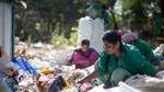 Women in green uniforms sort recyclable waste outdoors at a recycling facility.