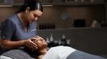 Spa therapist gently massages a client’s face in a treatment room with skincare products in the background