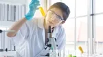 lady in science lab wearing lab coat looking at a yellow test tube