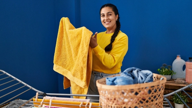 A women in yellow jumper doing laundry holding a yellow towel.