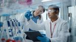 Male scientist and female scientist consider a flask of blue chemicals in a lab testing environment.
