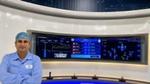 Factory engineer in protective gear stands before large digital dashboards showing production analytics.