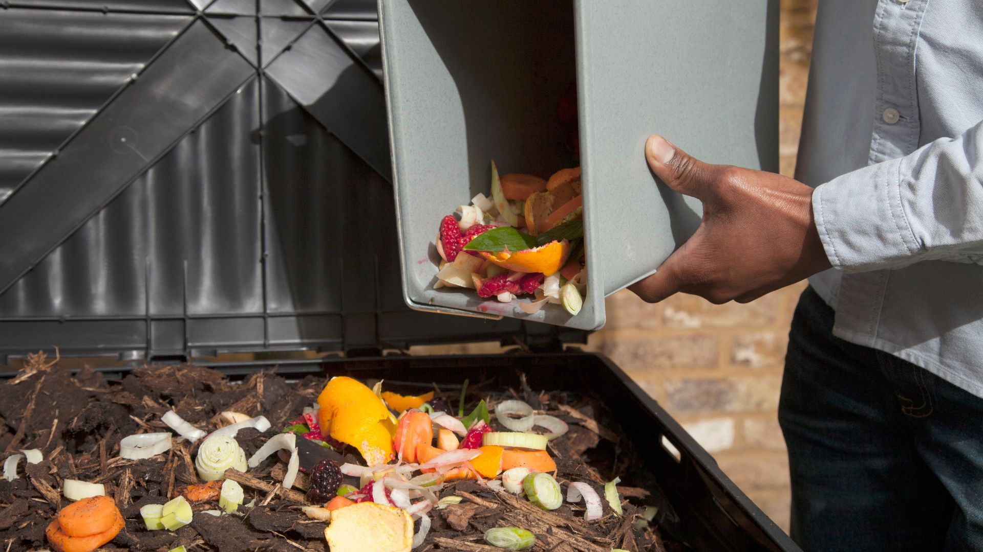 Cropped person emptying a bin of food scraps into a bigger bin