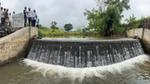 Community members inspect a small concrete check dam with water flowing over the edge.