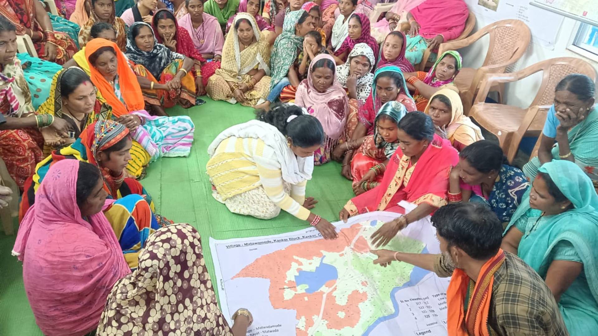 Group of women and a man discussing a large map on the floor.