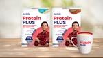Two packs of Horlicks Protein Plus packs in vanilla and chocolate flavours featuring a man in a red shirt, along with a filled mug displayed on a wooden surface.