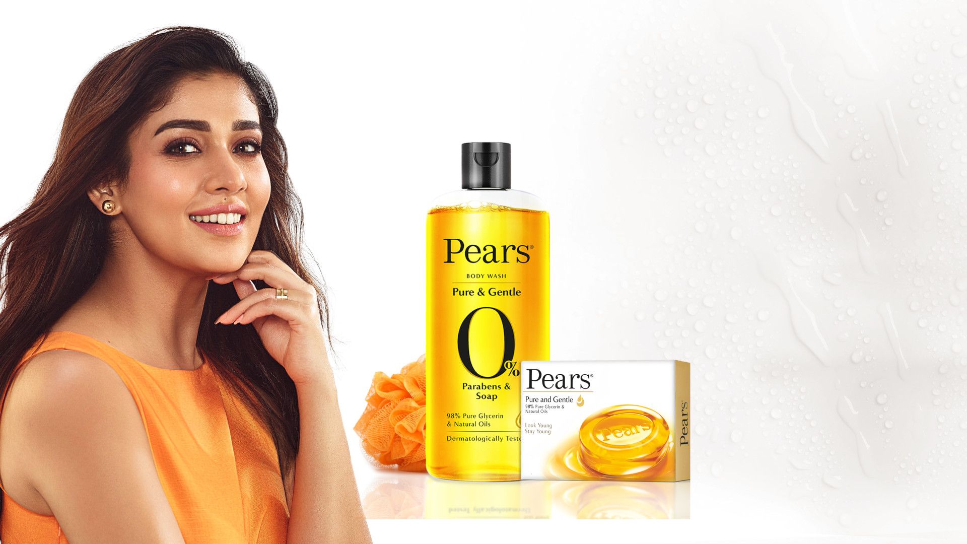 A woman posing with a smile in orange top next to Pears packaging
