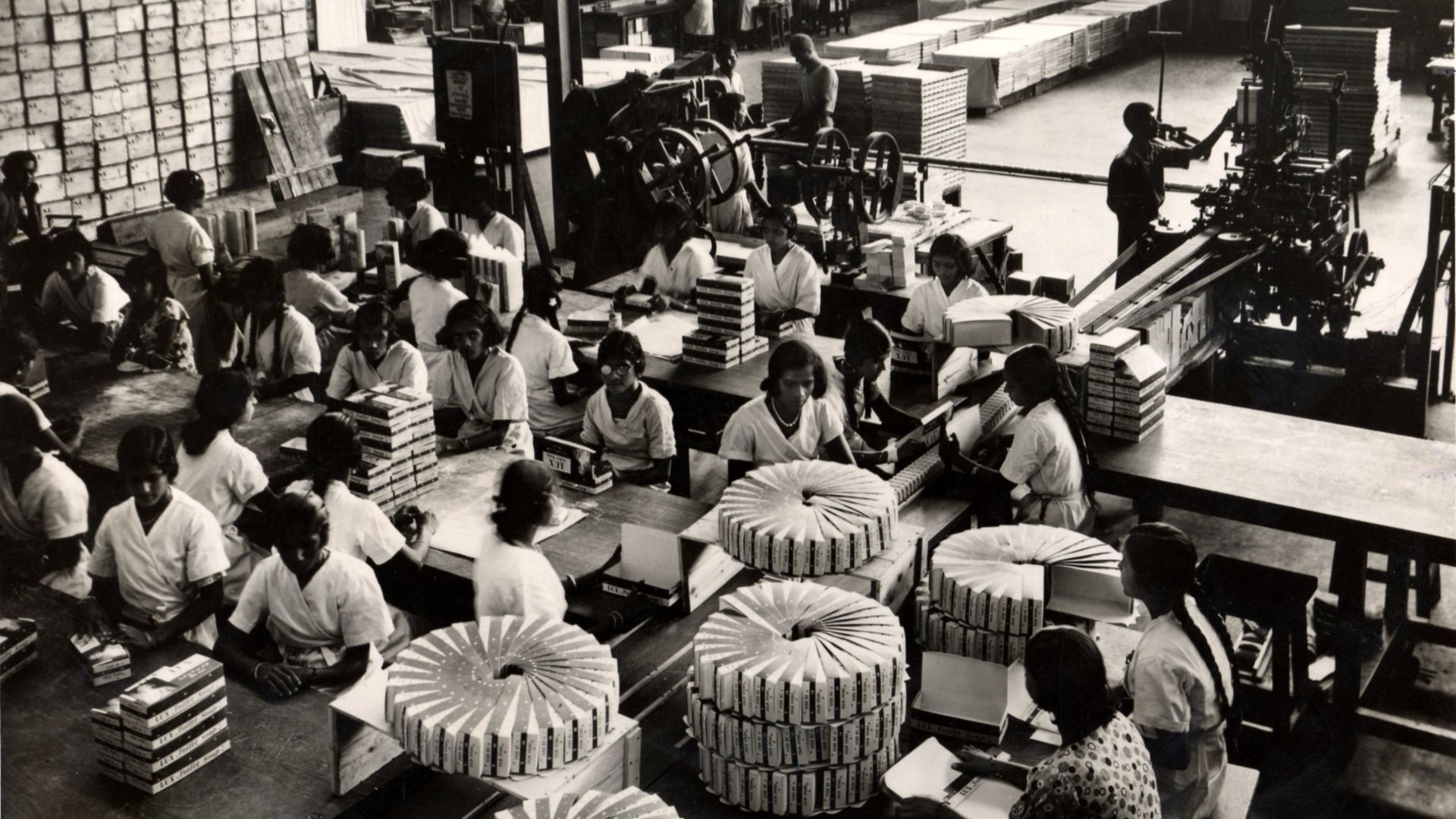 Workers package products along assembly lines in a busy factory.