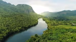 An image of a lush green forest surrounding a river with mountains on both sides connected to the valley.