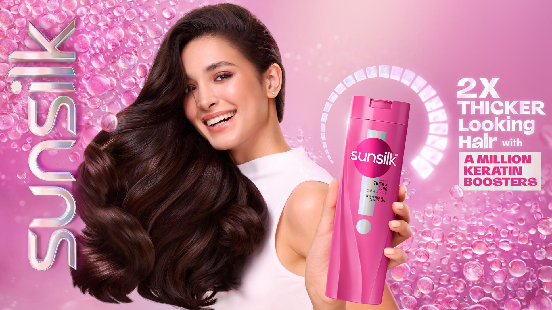 A woman with thick, flowing brown hair smiles, holding a pink Sunsilk shampoo bottle.