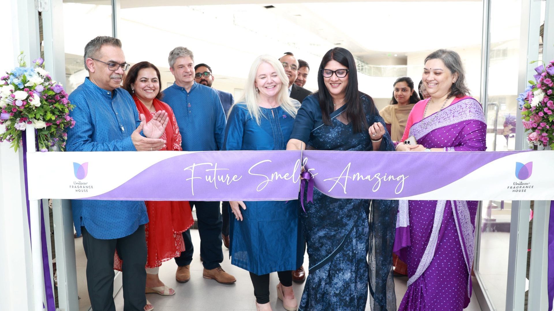 Group of people cutting a ribbon at an event, standing behind a banner that reads “Future Smells Amazing”.