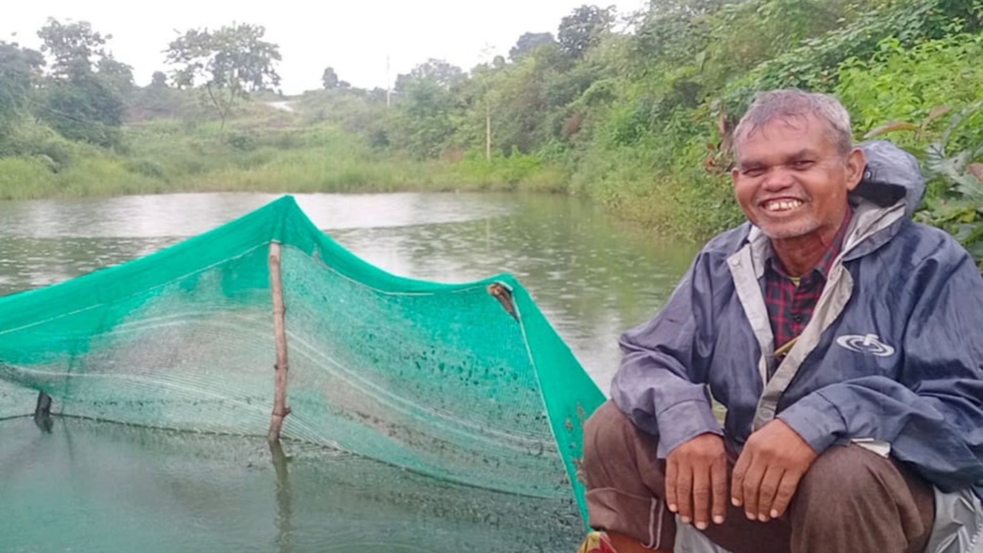 A man sitting beside a rainwater storage pond and a harvesting pit.