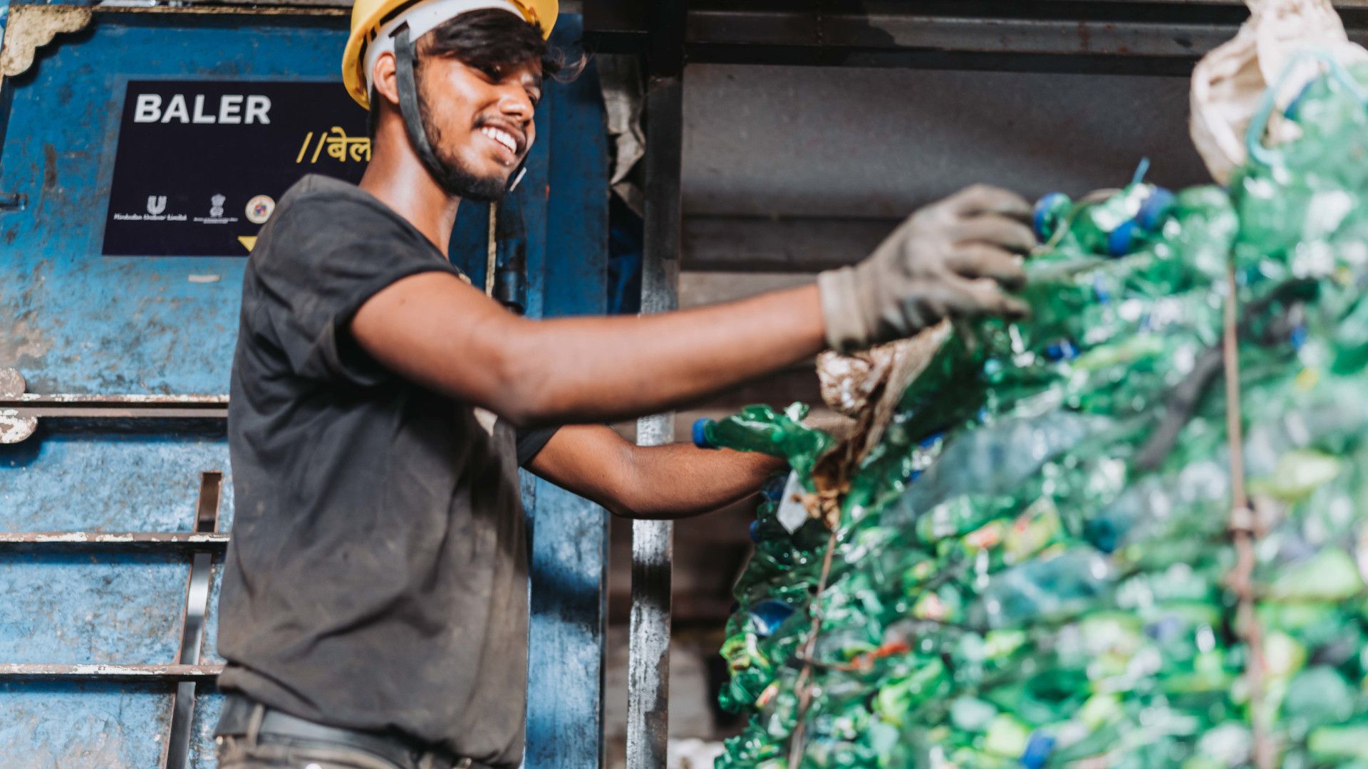 A worker in a hard hat and gloves smiles while arranging plastics