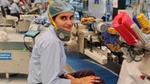 Worker in uniform and hairnet seated near machinery in factory.