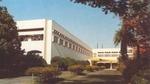 White corporate building surrounded by landscaped gardens and mature trees