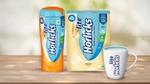 Horlicks Lite nutrition drink in regular malt and badam flavours, along with a branded white mug with Horlicks Lite is shown filled with the drink.